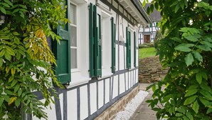 A traditional half-timbered house with green shutters and a stone wall. - Apartment in the half-timbered courtyard 'house in motion' (Neunkirchen-Seelscheid)