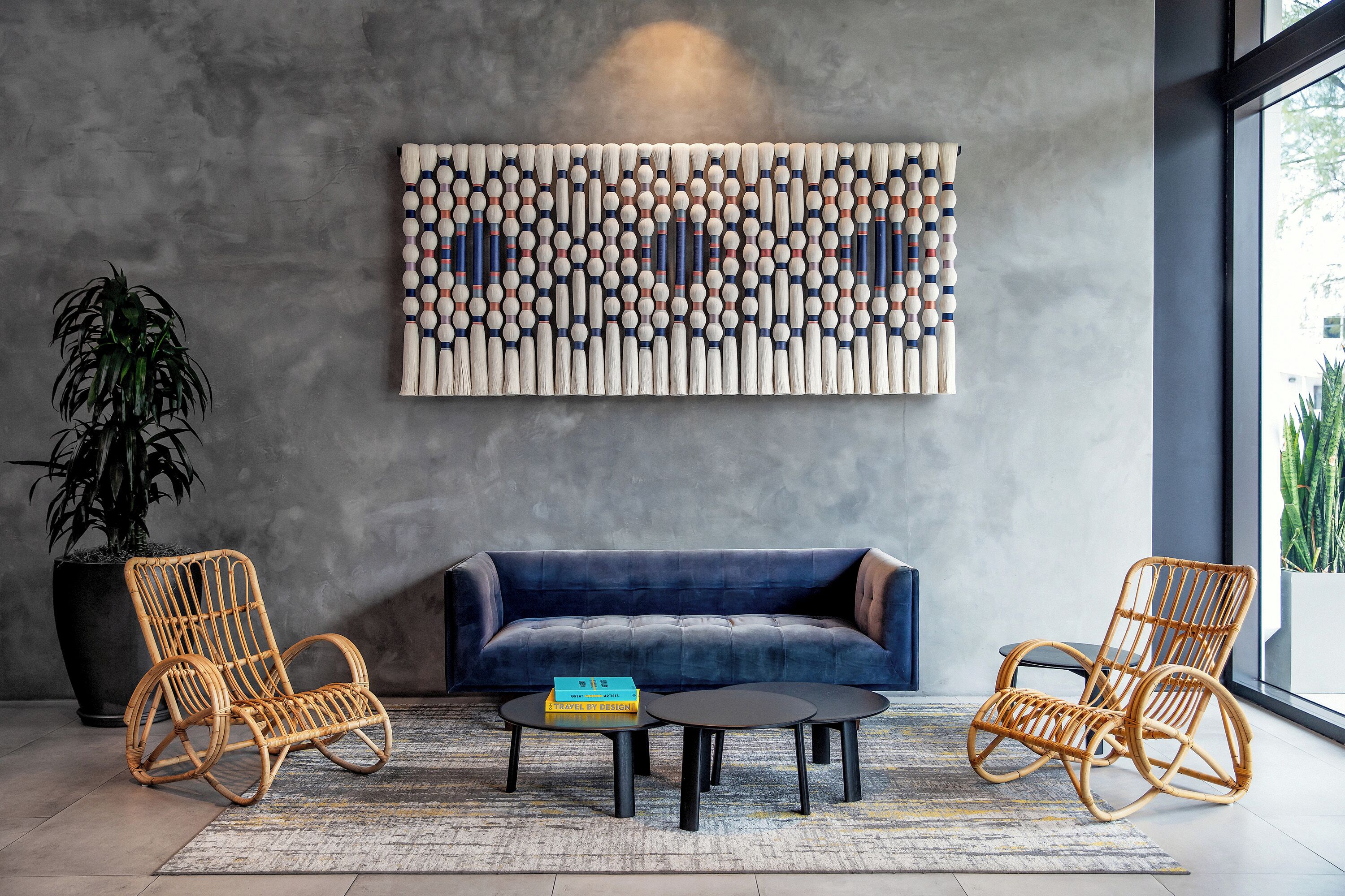 A modern living room with a blue sofa, two wicker chairs, a coffee table, and a decorative wall piece.