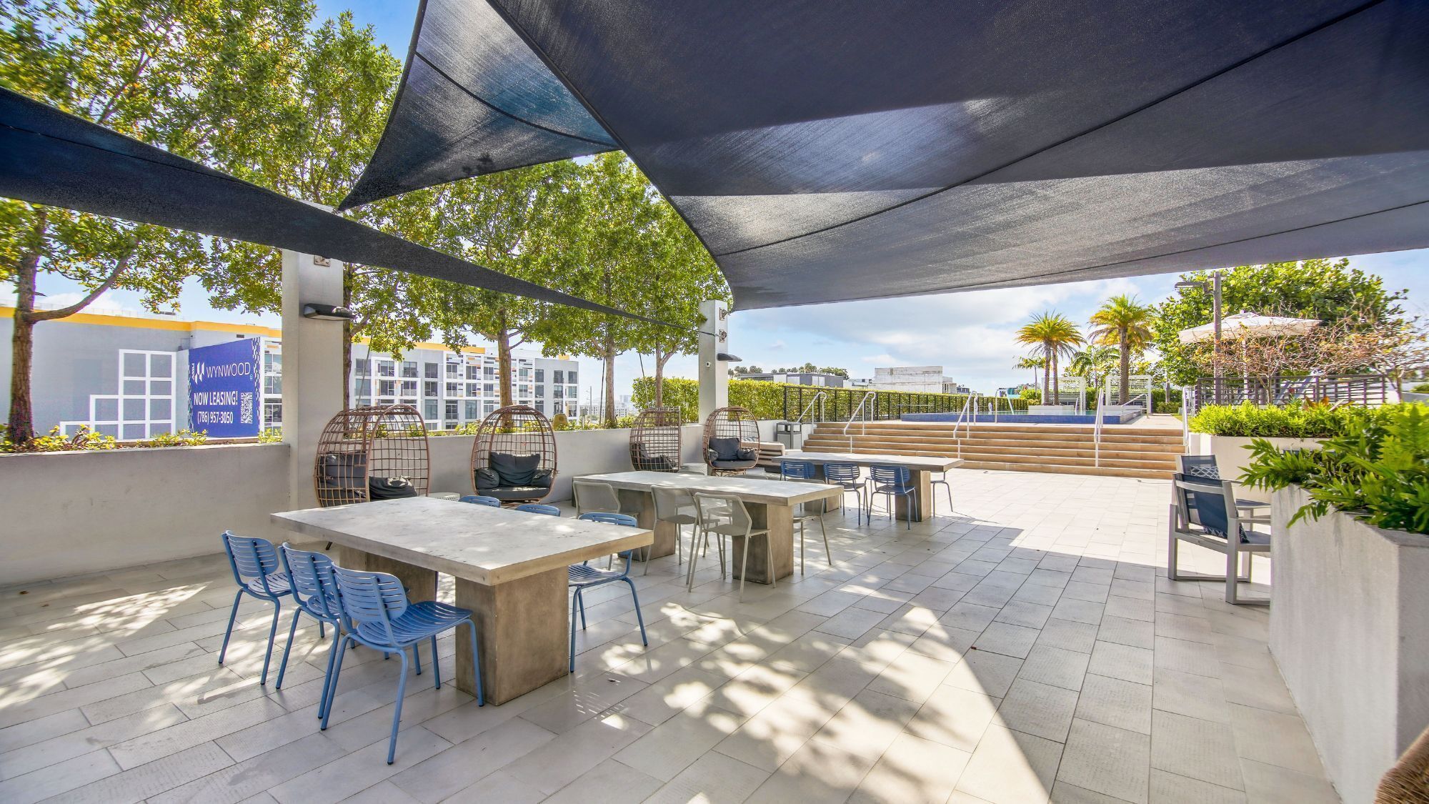 Ein Terrassenbereich im Freien mit Tisch und Stühlen, eine Sitzecke mit einer Schaukel und Blick auf ein Gebäude im Hintergrund.