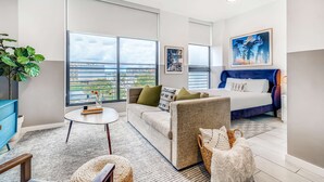A modern hotel room with a large window, a sofa, a bed, and a small table. - Sentral Wynwood (Miami)