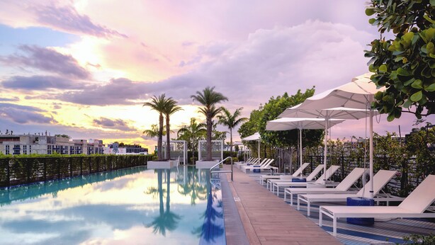 A swimming pool with lounge chairs and umbrellas, surrounded by greenery and buildings. - Sentral Wynwood (Miami)