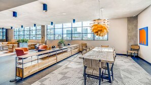 A spacious lounge area with a long wooden bench, a dining table, and modern seating. Large windows provide a view of the cityscape. - Sentral Wynwood (Miami)