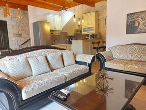 A living room with a sofa, a glass coffee table, and a kitchen in the background.