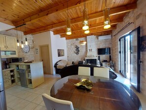 A spacious kitchen with wooden ceiling beams, a stone wall, and a large dining table with chairs.