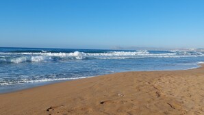 Ein Strand mit Wellen, einem klaren Himmel und sanften Hügeln in der Ferne.