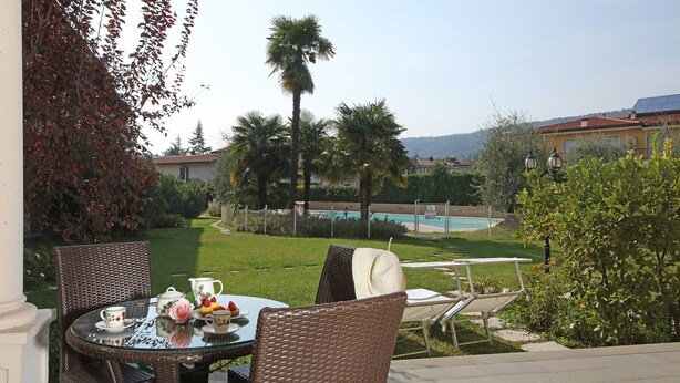 An outdoor seating area with wicker chairs and a glass table, overlooking a swimming pool and lush greenery. - Il Cedro - near to the old town of Salò with pool (Salò)