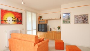 A living room with orange furniture, a TV, and artwork on the walls. - Il Cedro - near to the old town of Salò with pool (Salò)