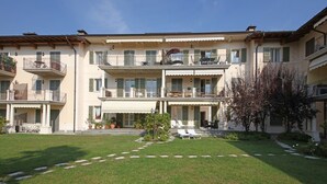 A multi-story building with balconies, a central courtyard with lounge chairs, and potted plants. - Il Cedro - near to the old town of Salò with pool (Salò)