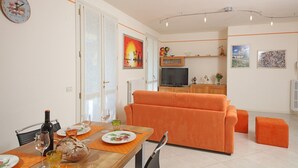 A modern living room with a sofa and a dining area with a table set for two. - Il Cedro - near to the old town of Salò with pool (Salò)