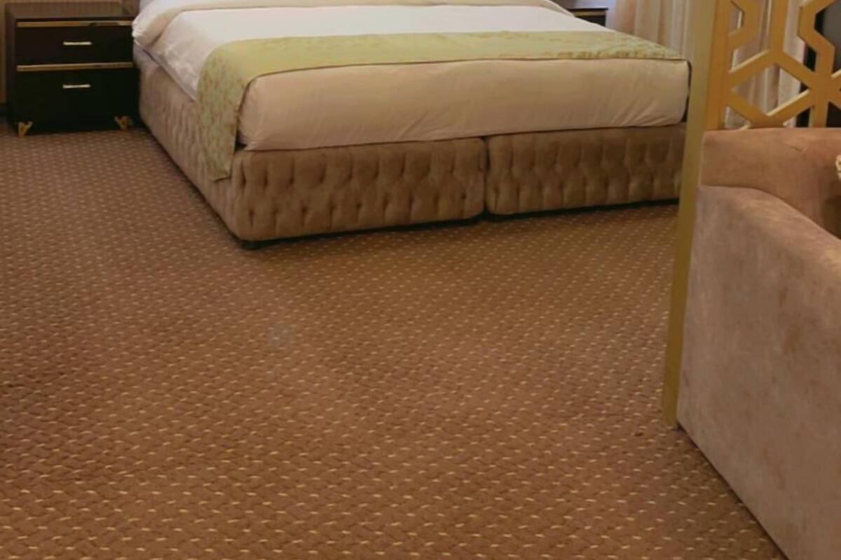 A hotel room with a large bed, a nightstand, a wooden headboard, and a patterned carpet.