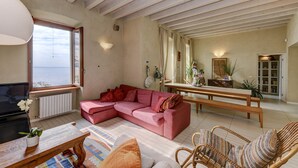 Un salon spacieux doté d’une grande fenêtre, d’un canapé d’angle, d’un banc en bois et d’un fauteuil en osier.