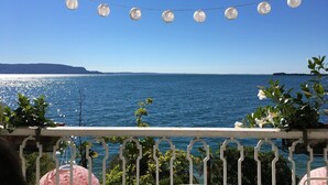 Un balcon avec vue sur la mer, des guirlandes lumineuses et quelques plantes.