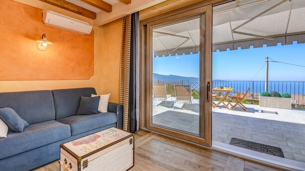 A room with a blue sofa, a wooden chest, and a sliding glass door leading to an outdoor area with a table and chairs.
