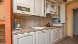 A kitchen with white cabinetry, a granite countertop, a coffee machine, a microwave, and a sink.