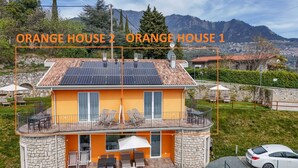 A two-story house with a yellow facade and a balcony, solar panels on the roof, and a stone foundation. - Orange House with breathtaking lake view (Tignale)