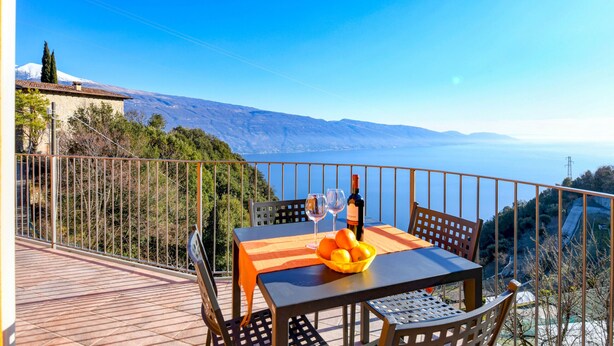 A table with a bottle, glasses, and oranges on a balcony overlooking a mountainous landscape. - Orange House with breathtaking lake view (Tignale)