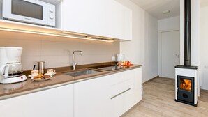 A modern kitchen with white cabinets, a microwave, a coffee maker, and a wood-burning stove. - Orange House with breathtaking lake view (Tignale)