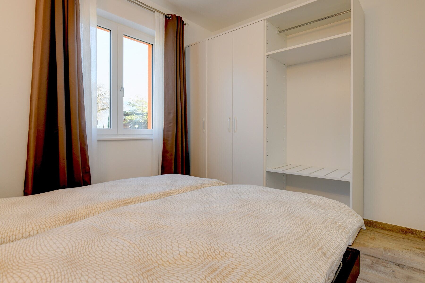 A bedroom with two beds, a wardrobe, and a window with curtains.
