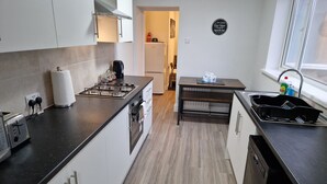 A modern kitchen with white cabinets, a black countertop, a gas stove, a coffee maker, and a sink with a dish rack. - Birtley's Diamond 3 bed Apt, Sleeps 6 Guests (Chester-le-Street)