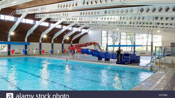 An indoor swimming pool with a clear water surface, a red and blue water slide, and a person standing near the slide. - Birtley's Diamond 3 bed Apt, Sleeps 6 Guests (Chester-le-Street)