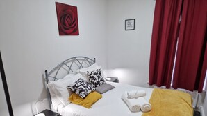 A neatly made bed with pillows, a bedside lamp, a small nightstand, a red curtain, and a framed quote on the wall. - Birtley's Diamond 3 bed Apt, Sleeps 6 Guests (Chester-le-Street)