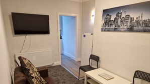 A living room with a brown leather sofa, a white table, and two black chairs. A flat-screen TV is mounted on the wall above the sofa. - Birtley's Diamond 3 bed Apt, Sleeps 6 Guests (Chester-le-Street)