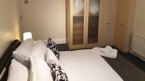 A hotel room with a bed, two pillows, a bedside lamp, a wardrobe, and a rolled-up towel on the floor. - South Shield's Emerald 2 Bed Apartment (South Shields)