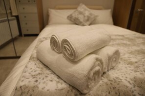 A neatly made bed with rolled white towels and a patterned bedspread. - South Shield's Emerald 2 Bed Apartment (South Shields)
