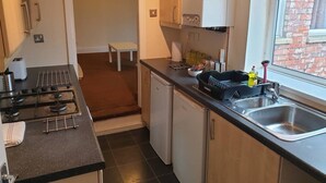 A compact kitchen with a gas stove, a sink, and white cabinets. There's a window with a view of a brick building. - South Shield's Emerald 2 Bed Apartment (South Shields)