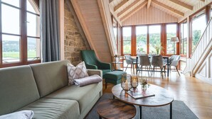 A cozy living room with a stone wall, a green armchair, a sofa, and a dining area with chairs and a table. - Ferienwohnungen Alte Destillerie Rathen (Rathen)