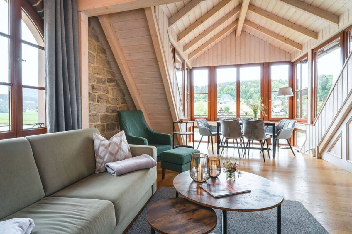 Ein gemütliches Wohnzimmer mit einer Steinwand, einem grünen Sessel, einer Couch und einem Essbereich mit Stühlen und einem Tisch.