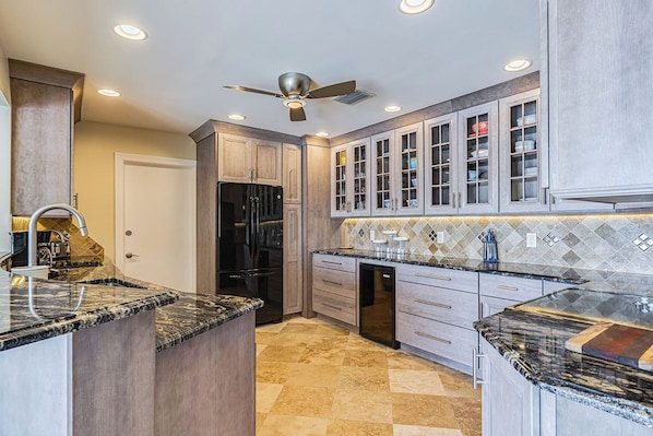 A kitchen with granite countertops, a black refrigerator, and wooden cabinets with glass doors.