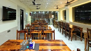 A dining area with wooden tables and chairs, ceiling fans, and a large window with a city view. - Hotel Star Palace (Jaipur)