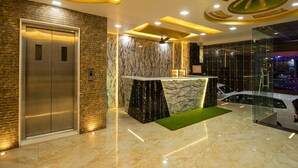A lobby with a marble reception desk, an elevator, and a glass wall with a view of parked cars. - Hotel Star Palace (Jaipur)