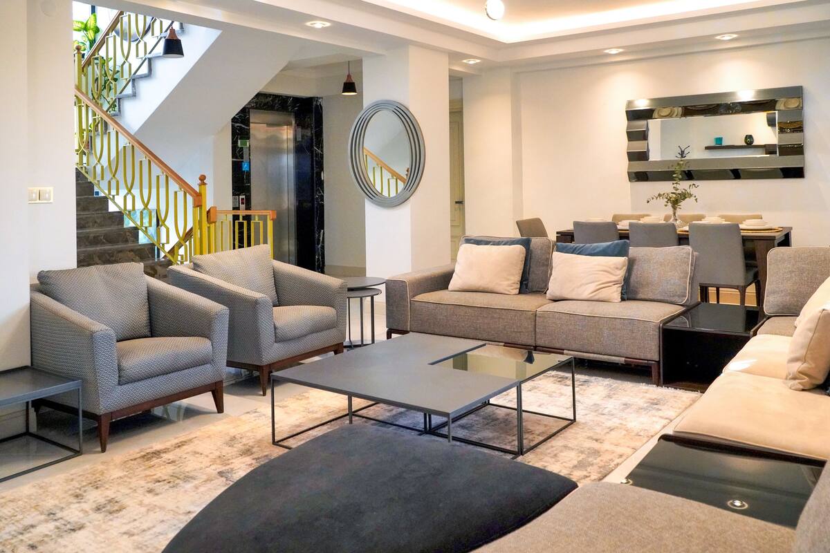 A modern living room with a sofa, armchairs, a coffee table, and a dining area with chairs and a table.