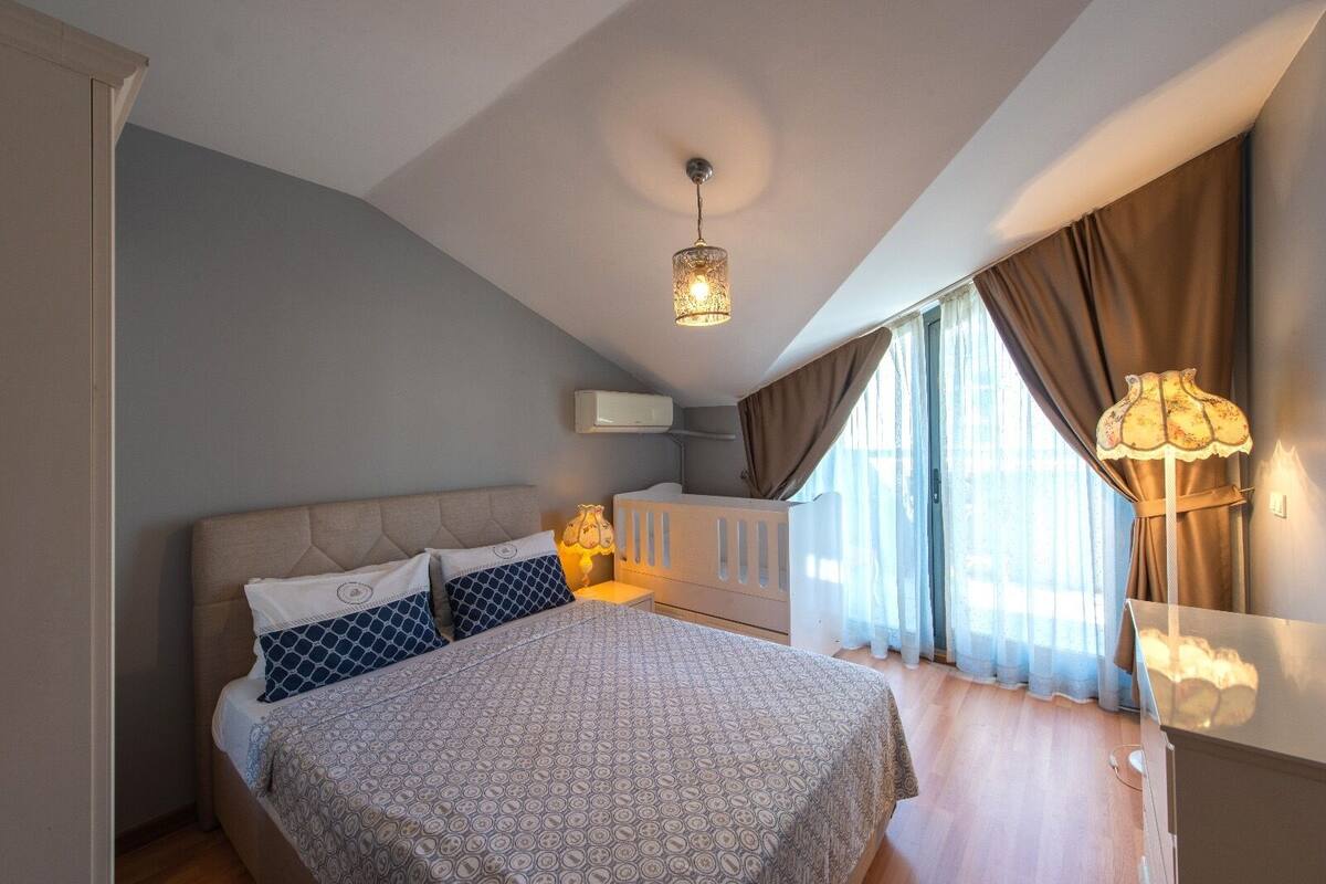 A bedroom with a large bed, a ceiling light, a nightstand, and a window with curtains.