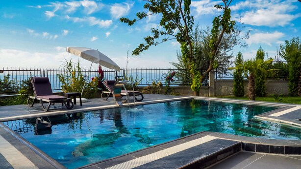 A swimming pool with lounge chairs and an umbrella, surrounded by greenery and a fence. - Taksim Elysium Residence CTS (Istanbul)