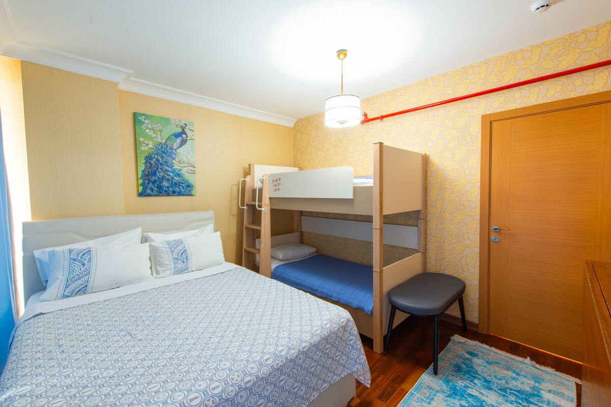 A bedroom with bunk beds, a single bed, a chair, a painting, and a door.