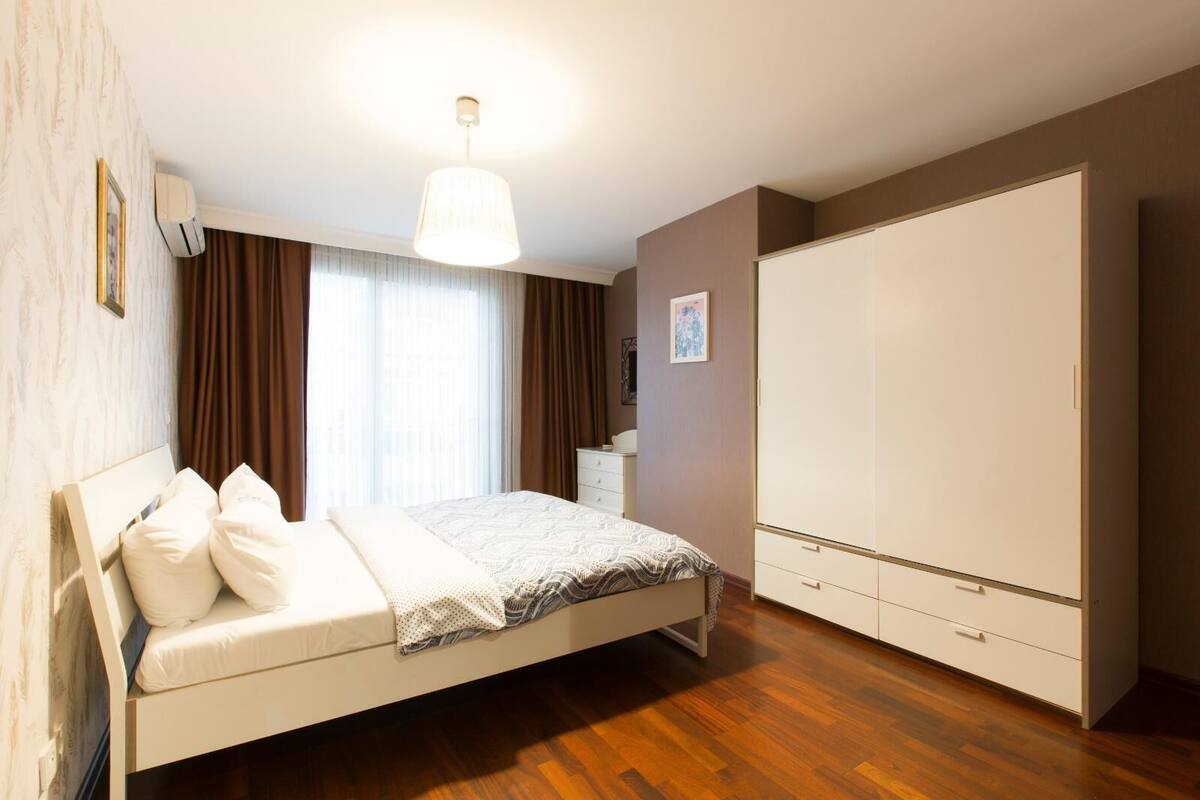 A bedroom with a bed, a wardrobe, a nightstand, and a window with curtains.