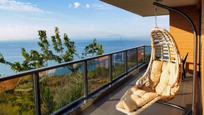 A balcony with a wicker chair, glass railing, and a view of the sea and hills. - Taksim Elysium Residence CTS (Istanbul)