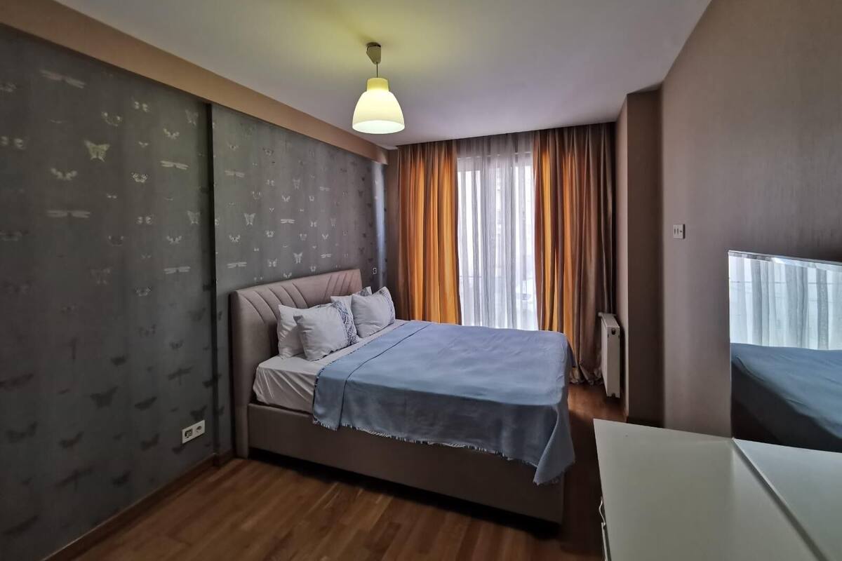 A bedroom with a bed, a radiator, a window with curtains, and a wall with a butterfly pattern.