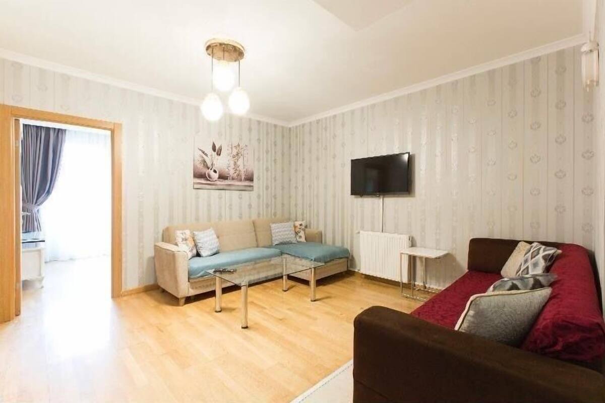 A living room with a sofa, a coffee table, and a TV mounted on the wall.