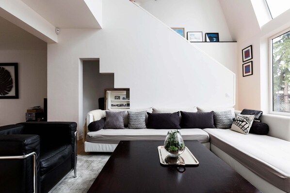 A modern living room with a sofa, a coffee table, and a black armchair. There is a staircase leading to an upper level.