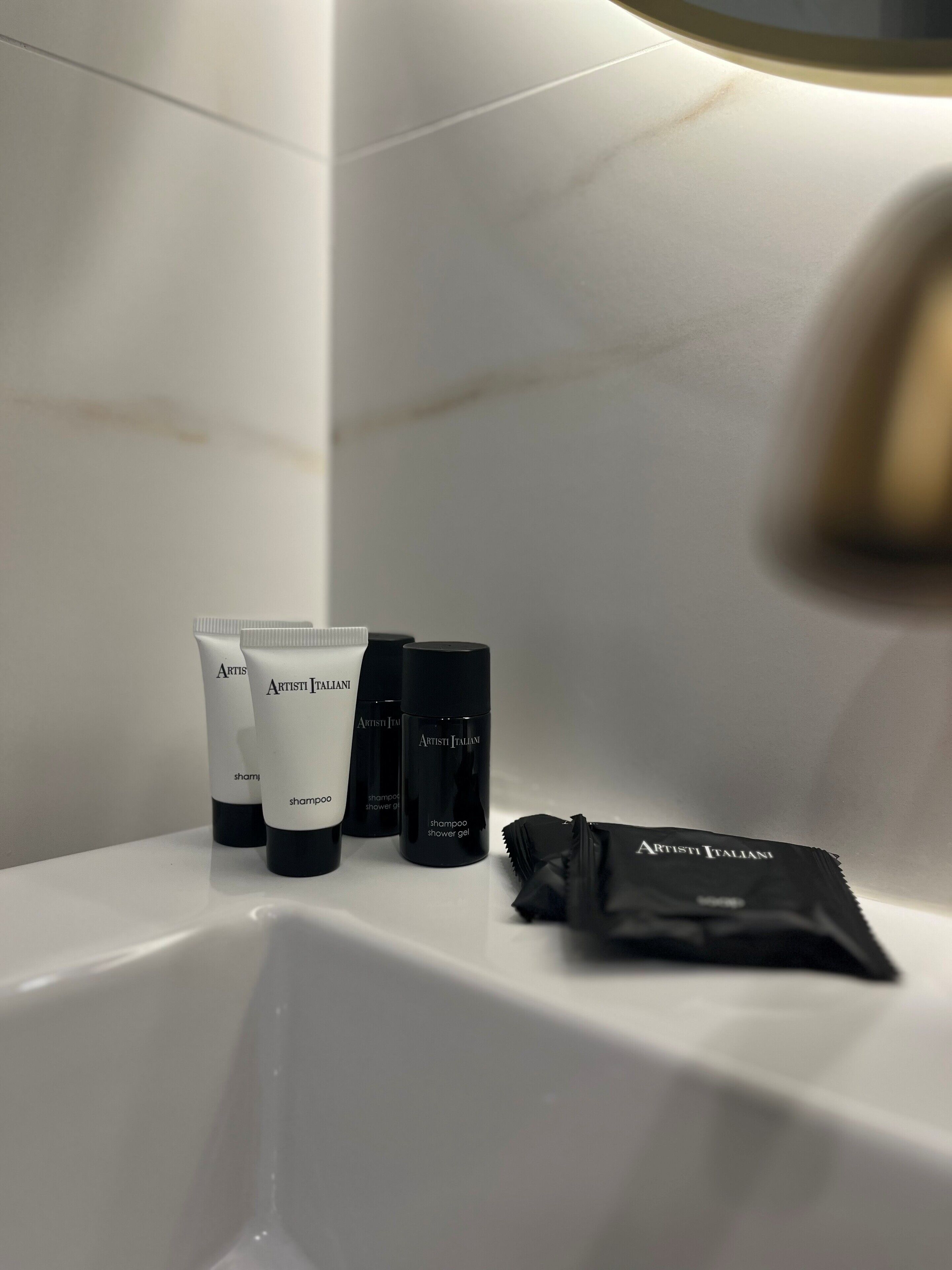 A bathroom with a white bathtub, three Artist Italian shampoo bottles, and a black shower bag.