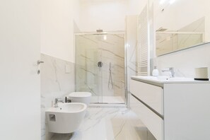 Une salle de bain moderne dotée d’une douche à parois de verre, d’un bidet, d’un lavabo et d’un miroir.