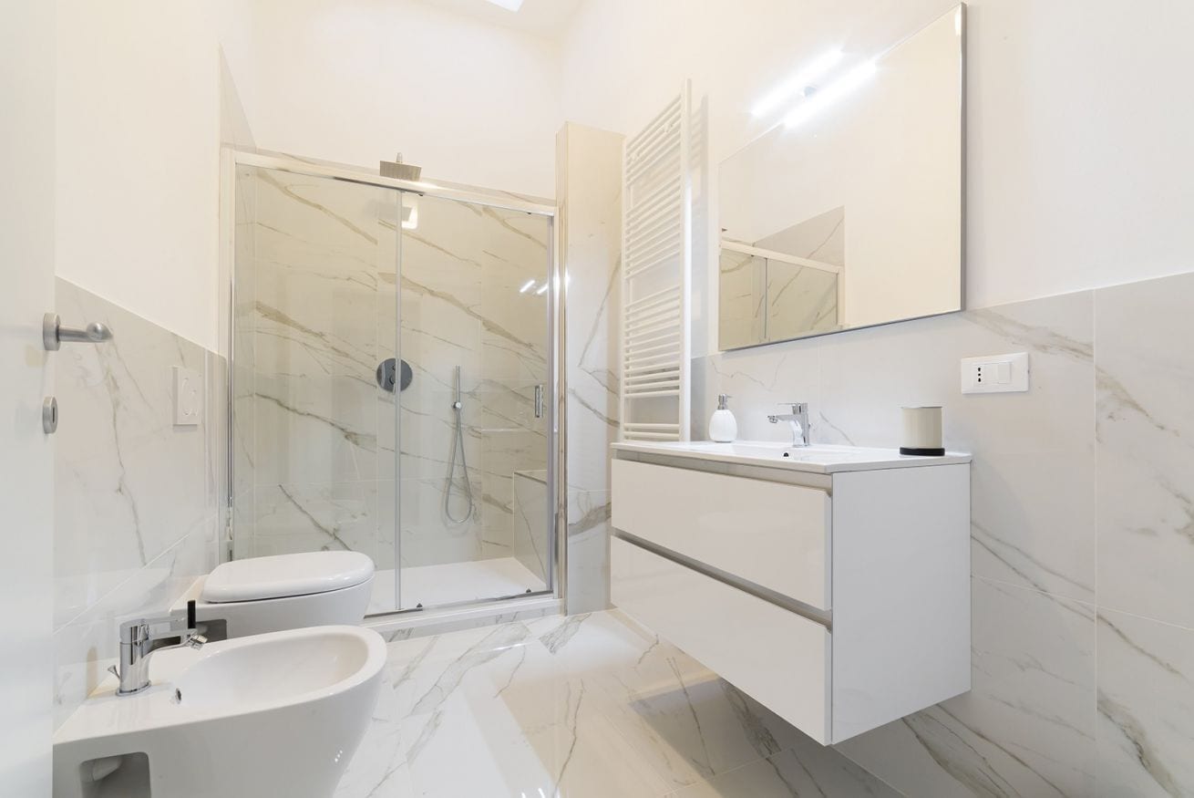 Un baño moderno con ducha envuelta en vidrio, inodoro blanco y tocador con espejo.