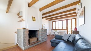 A living room with a stone fireplace, a black leather sofa, wooden beams, and a dining area with a table and chairs. - A delightful split level apartment with a beautiful terrace with view on the hills. (Firenze)
