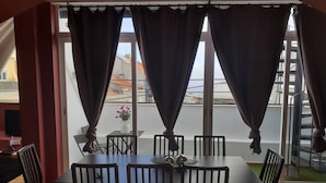 A dining area with a table and chairs, a vase with flowers, and a view of the street through large windows. - ALEXANDER APARTMENTS. LISBON (Lisboa)
