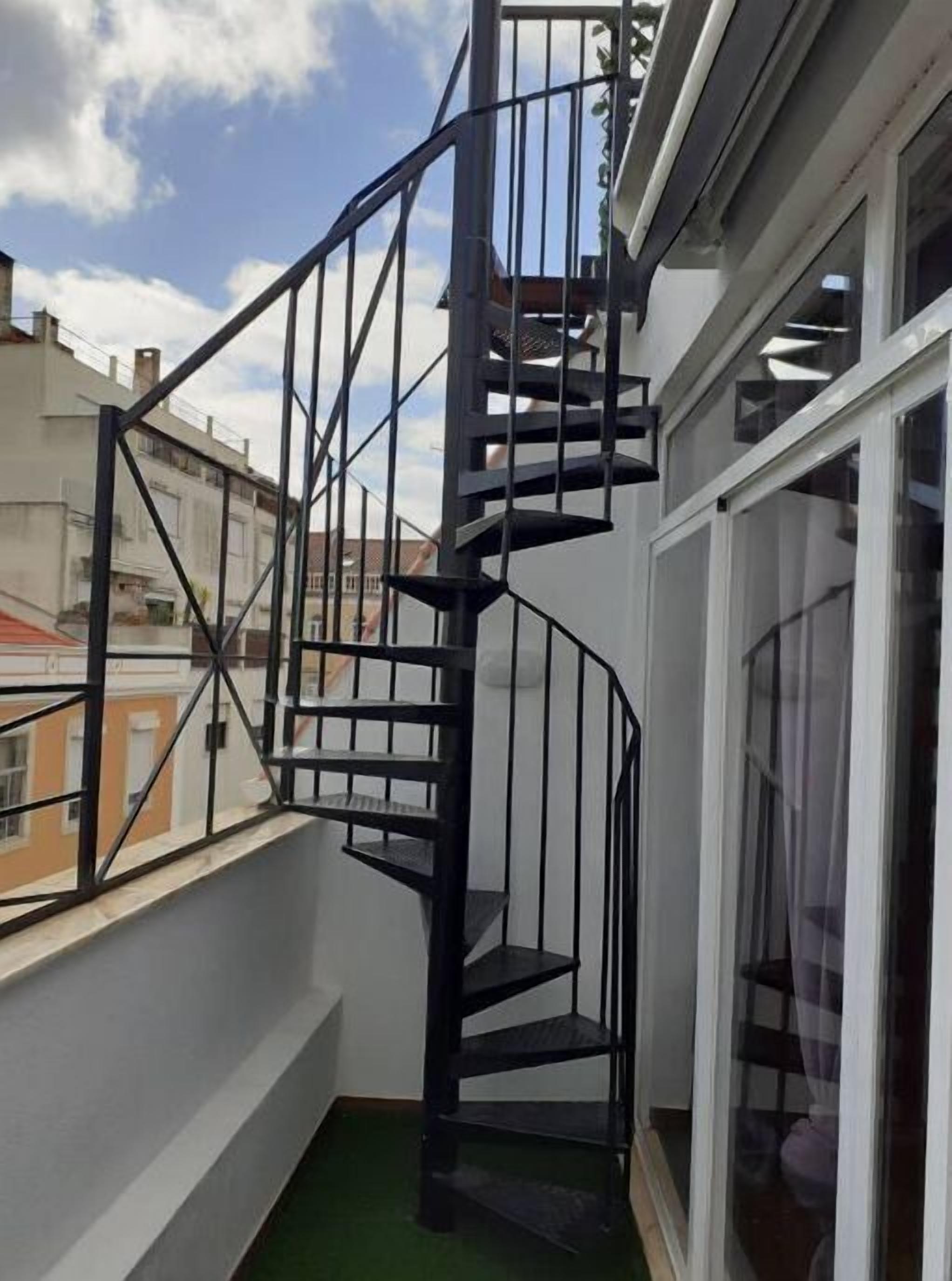 A black spiral staircase with a metal railing, leading to an upper floor.