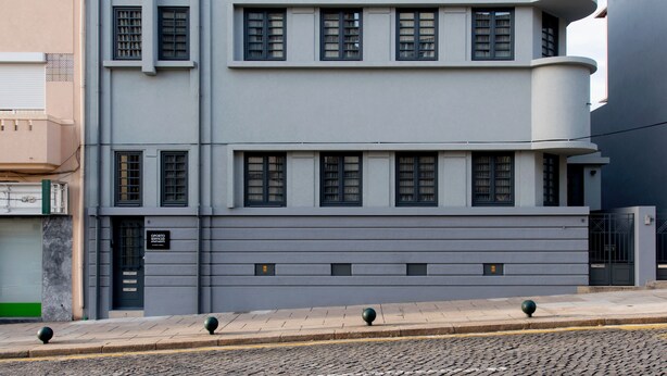 A multi-story building with a flat facade, large windows, and a curved balcony on the upper floor.